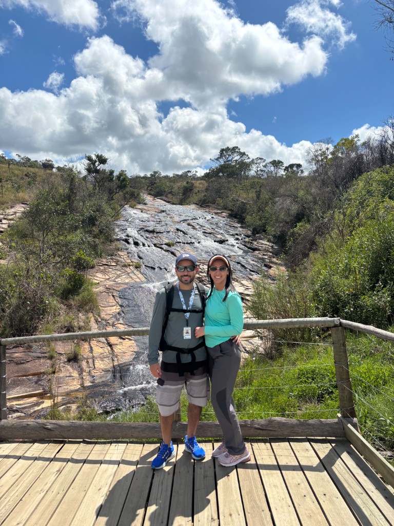 Casal em mirante de madeira com cachoeira e serra ao fundo