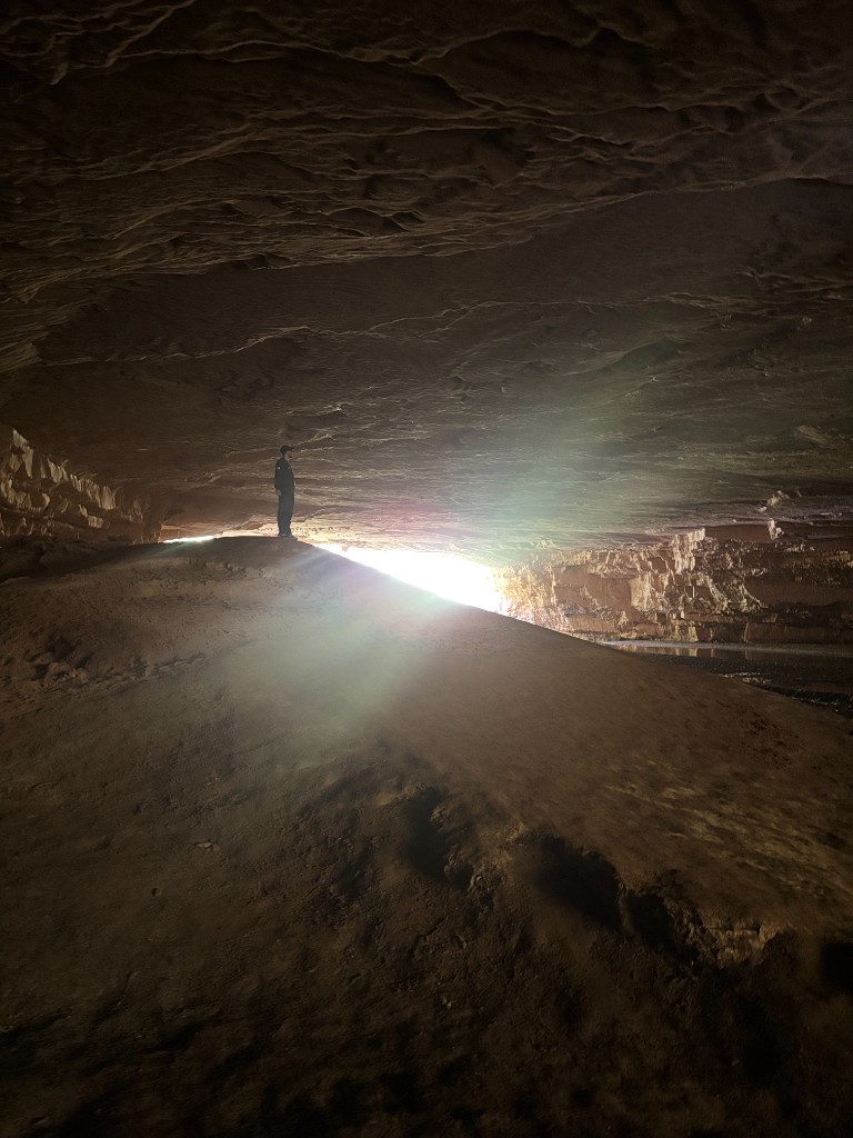 Trilheiro explorando gruta com luz natural entrando pela abertura