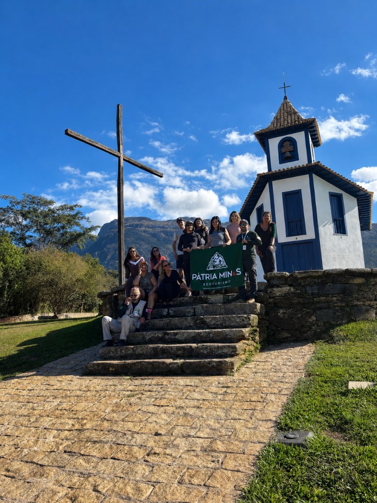 Grupo com a bandeira Pátria Minas em frente à capela colonial histórica