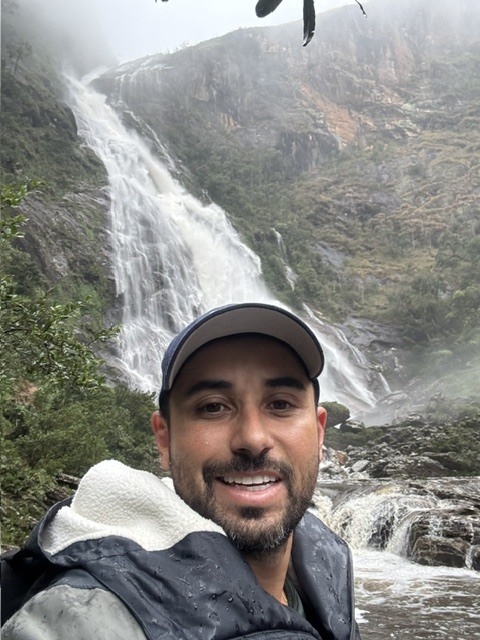 Trilheiro sorrindo em frente a uma grande cachoeira